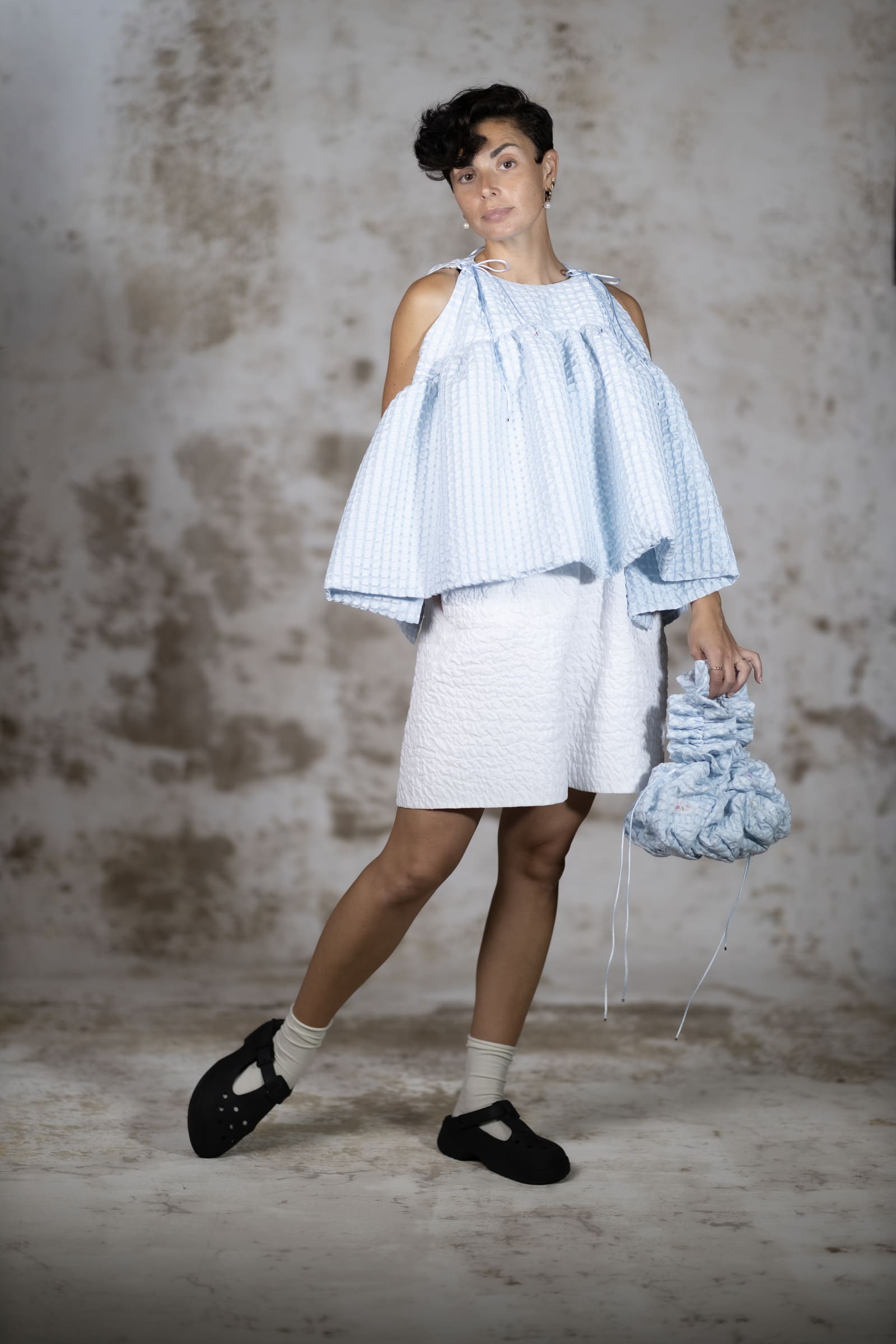 Full-body shot of the Blue Brisa blouse and the Brisa shorts, a voluminous structured top with dramatic ruffles and an alluring open back in rich light blue jacquard fabric - Anabel Santos