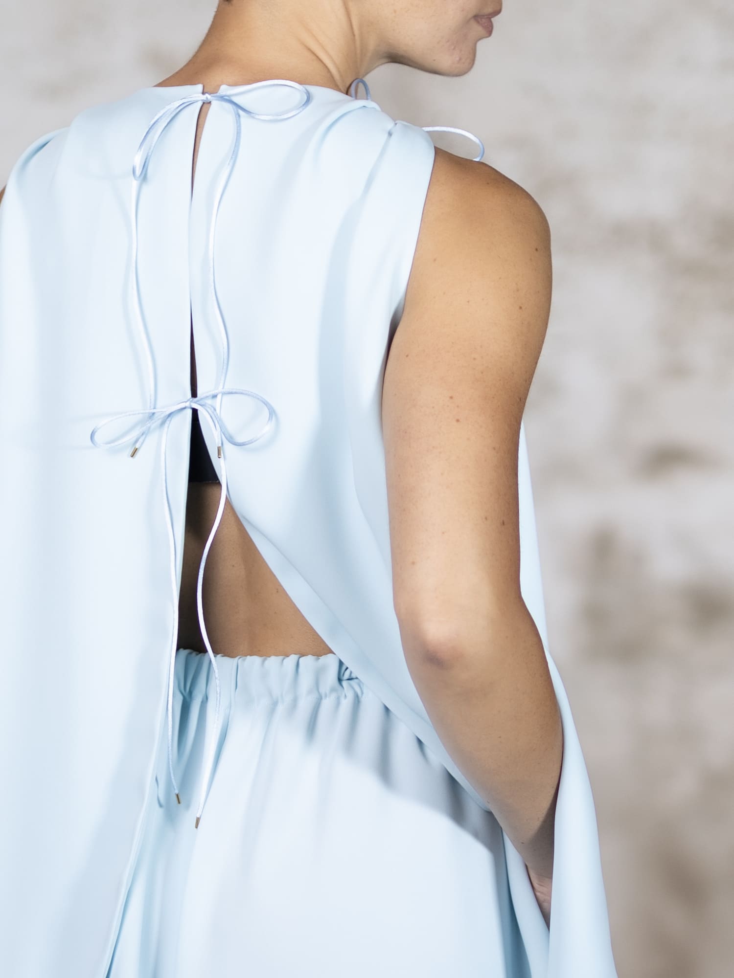 Full-body shot of a model presenting the Blue Area blouse, a fluid light blue crepe top showcasing an alluring dramatic open back with delicate double ties - Anabel Santos